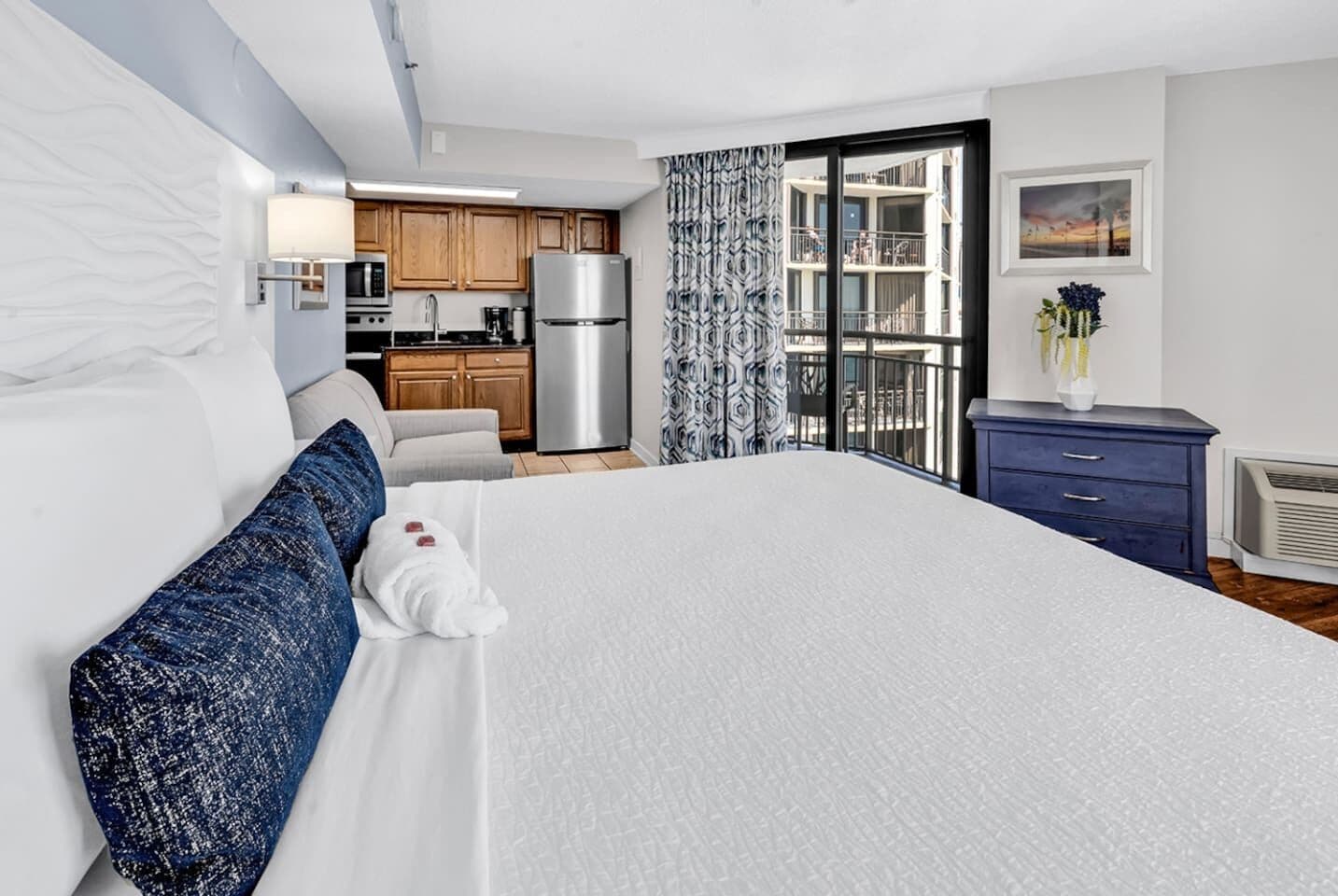 A hotel room with a large bed, a kitchenette, a bathroom, and a balcony with a view.