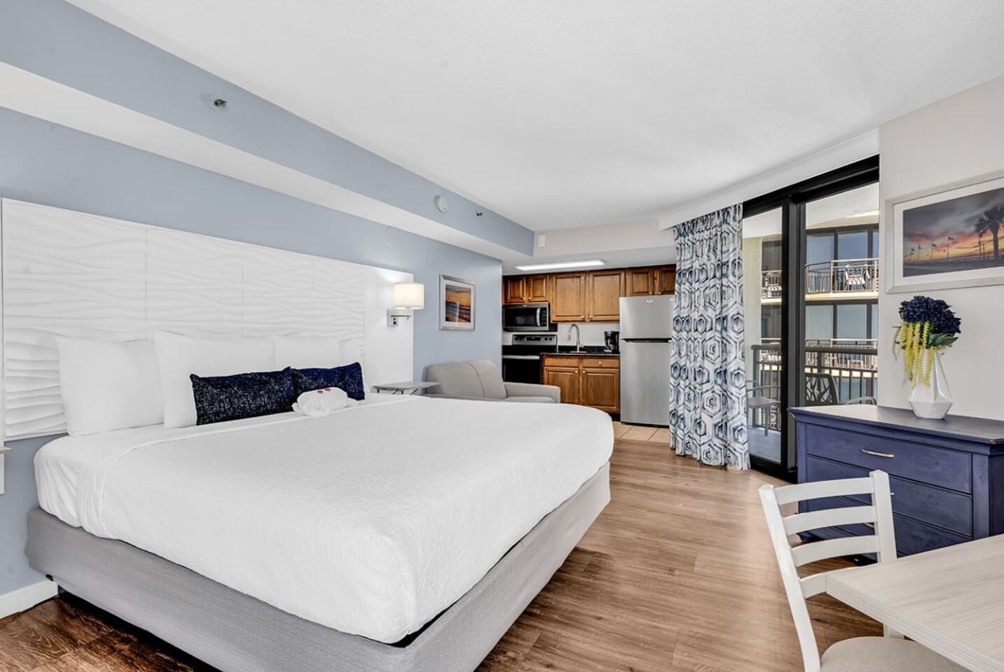 Ein modernes Hotelzimmer mit einem großen Bett, einer kleinen Küchenzeile und einem Balkon mit Blick.