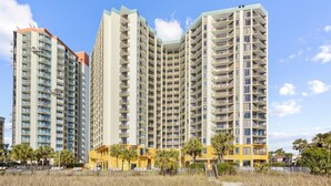 A high-rise residential building with multiple balconies, a central courtyard, and a pathway leading to the entrance. - Updated Oceanfront 16th floor w/ Amazing Views! (Myrtle Beach)