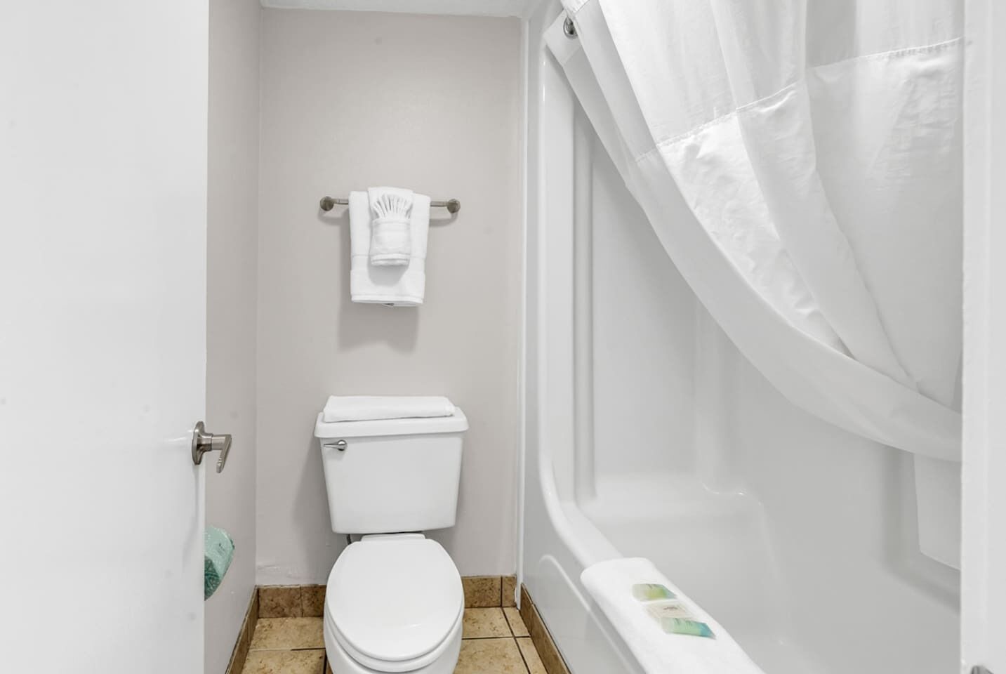 Une petite salle de bain blanche, équipée de toilettes, d’un porte-serviettes et d’un rideau de douche.