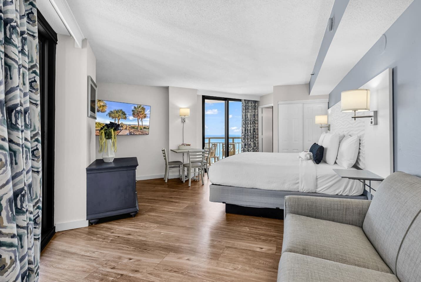 A hotel room with a large bed, a sofa, a desk, and a balcony with a view.