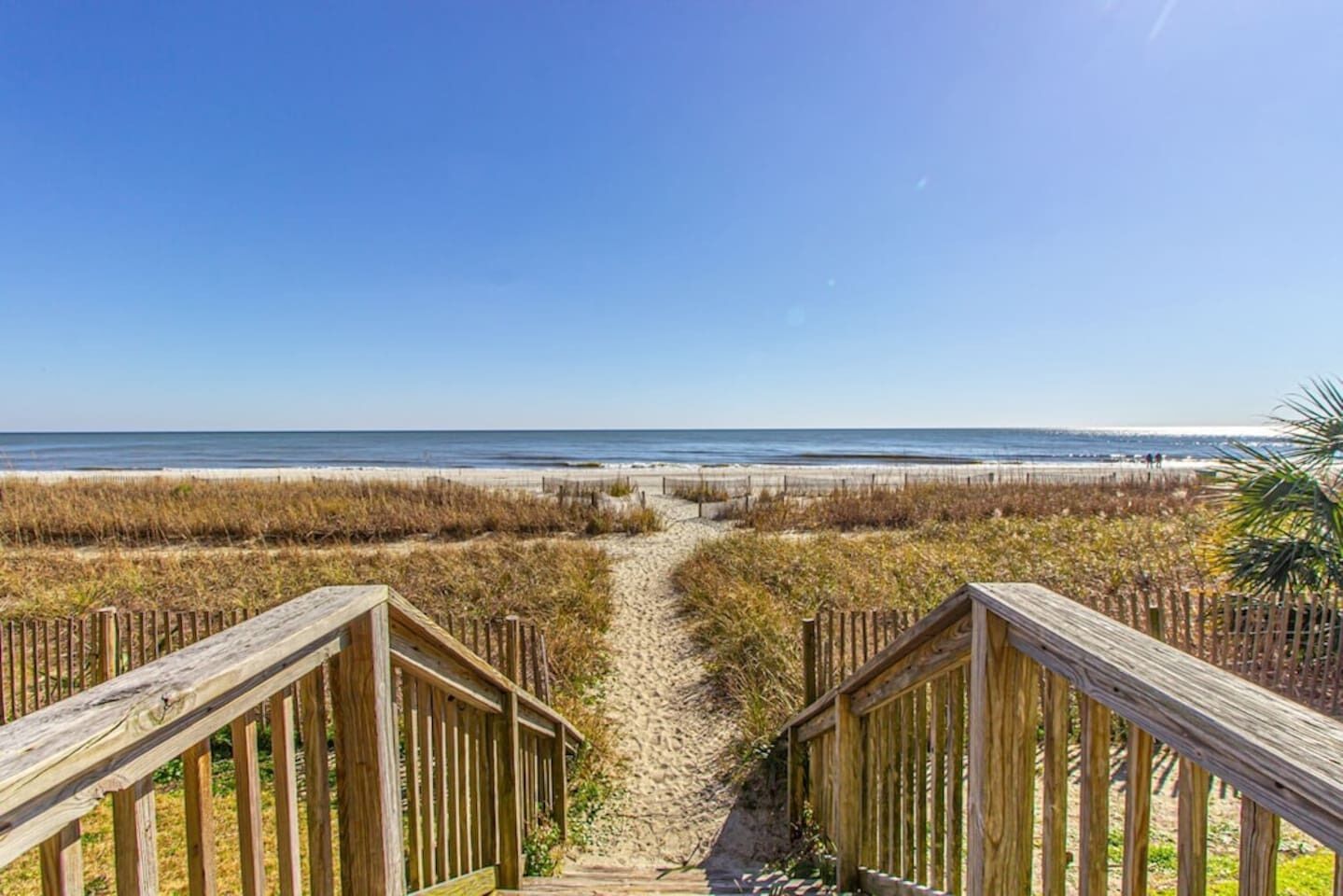 A wooden boardwalk leading to a beach with a clear view of the ocean.