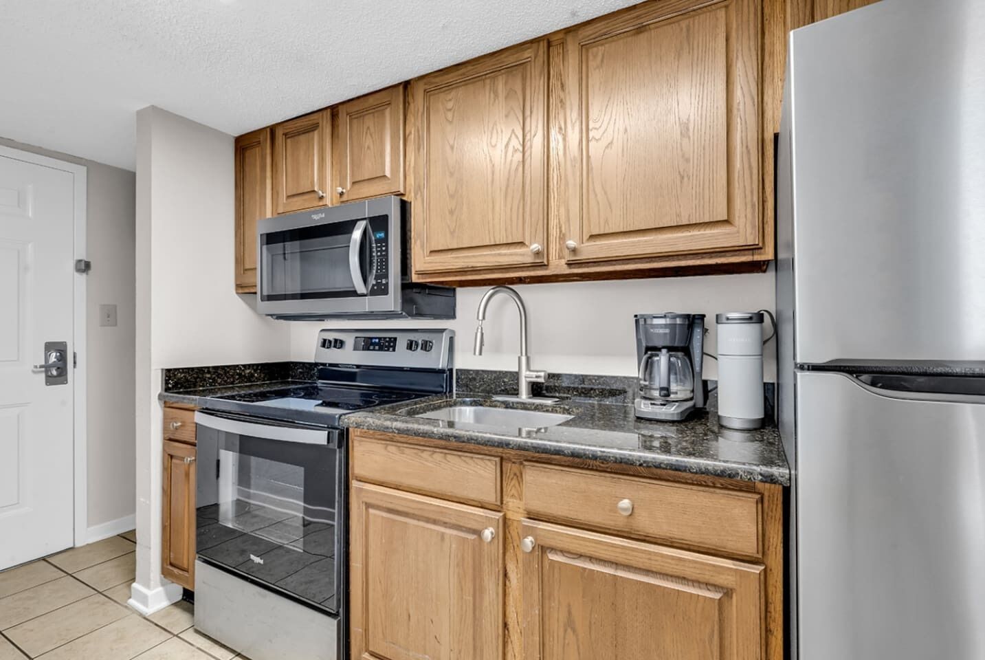 A modern kitchen with wooden cabinets, stainless steel appliances including a microwave, stove, and refrigerator, and a coffee maker on the countertop.