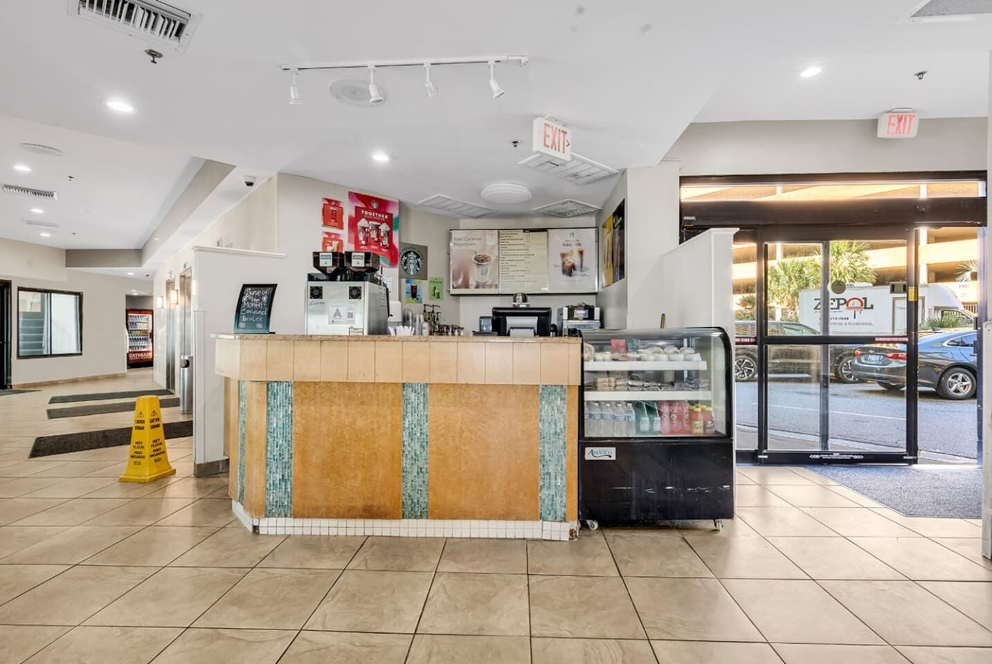 A clean, modern coffee shop interior with a counter, espresso machine, and a refrigerated display case.