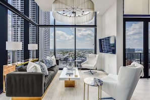 Uma sala de estar moderna com uma janela ampla, um sofá branco, uma mesa de centro e uma poltrona branca.