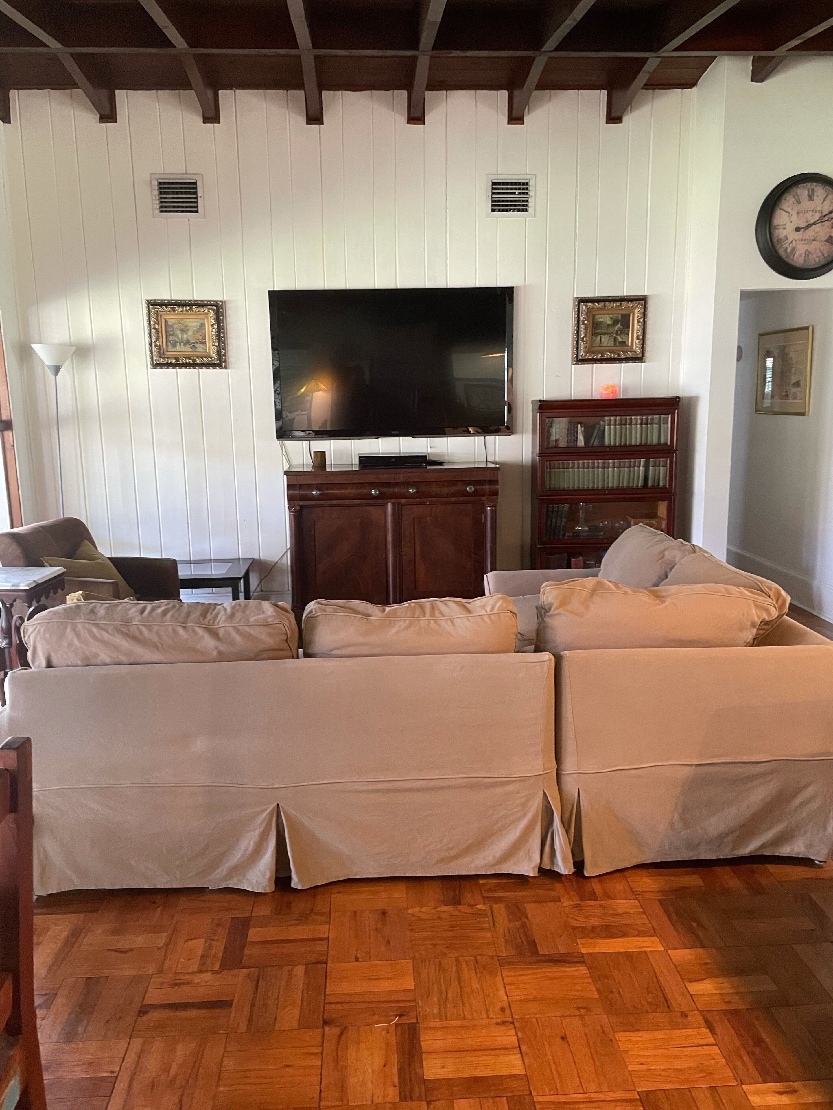 A living room with a sectional sofa, a flat-screen TV, a wooden cabinet, and a bookshelf.