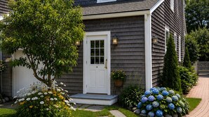A two-story house with a front door, a chimney, and a garden with flowers and a tree. - 29 India House (Nantucket)