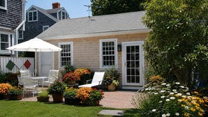 A house with a brick patio, white outdoor furniture, and a variety of potted plants and flowers. - 29 India House (Nantucket)