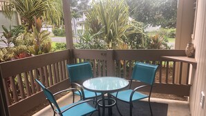 A covered outdoor seating area with a round table and four blue chairs, surrounded by a wooden fence and lush greenery. - Sandpiper 133B - updated and renovated studio in Princeville  (Princeville)