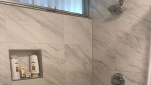 A shower area with a marble wall, a showerhead, and a shelf with toiletries. - Sandpiper 133B - updated and renovated studio in Princeville  (Princeville)