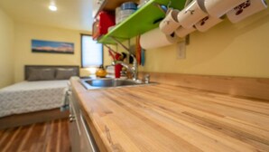Une cuisine compacte dotée d’un plan de travail en bois, d’un évier et d’une étagère verte sur laquelle sont posées des tasses blanches.