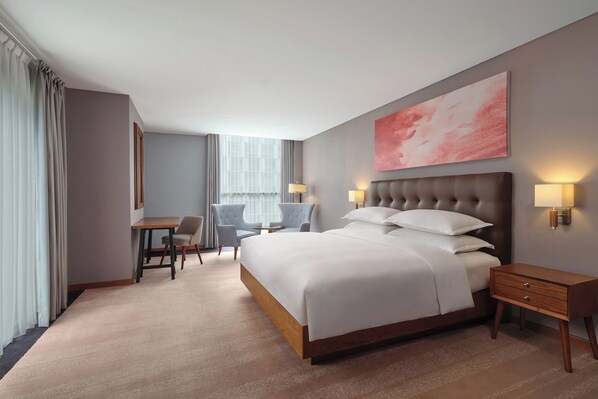 Una habitación de hotel con una cama grande, mesitas de noche, un escritorio y sillas.