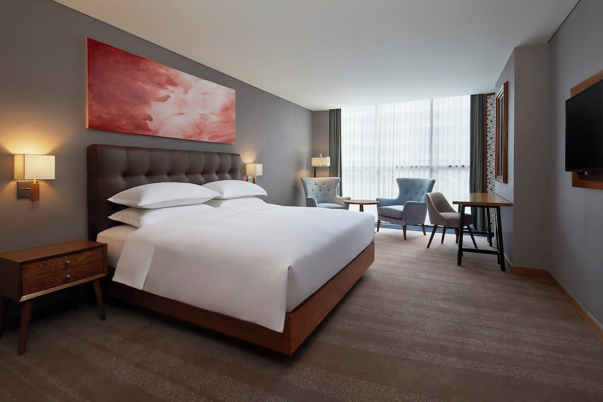 Une chambre d’hôtel avec un grand lit, des tables de chevet, un bureau, des chaises, une télévision et une grande fenêtre avec des rideaux.
