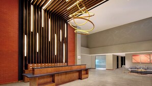 Een moderne lobby met een houten receptiebalie, verticale lichtpanelen en een hanglamp.