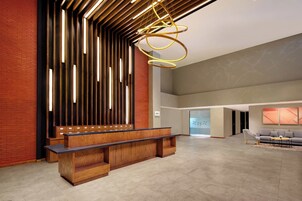 Un vestíbulo moderno con un mostrador de recepción de madera, paneles de luz verticales y una lámpara colgante.