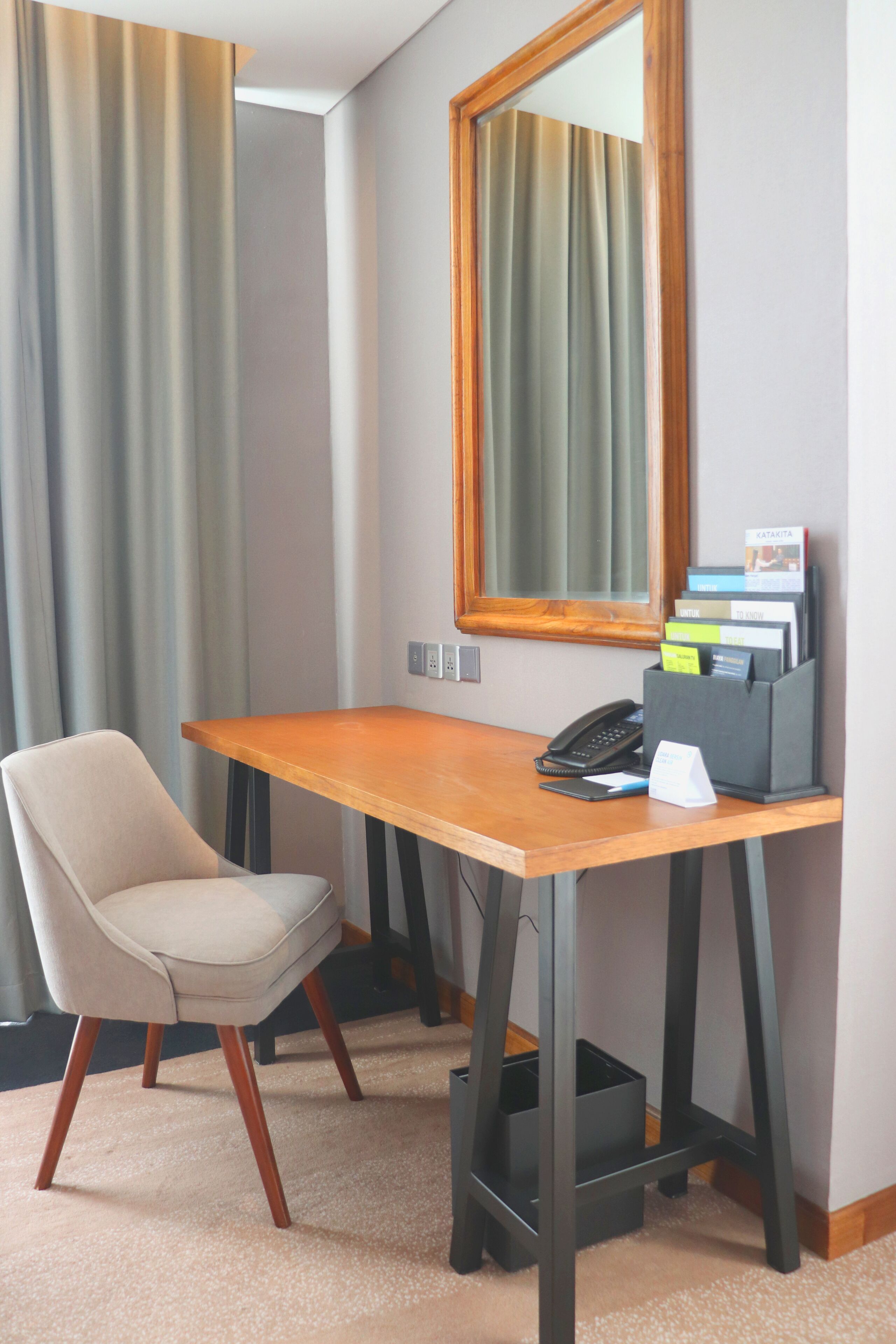 Una habitación de hotel con un escritorio de madera, una silla, un teléfono y un espejo.