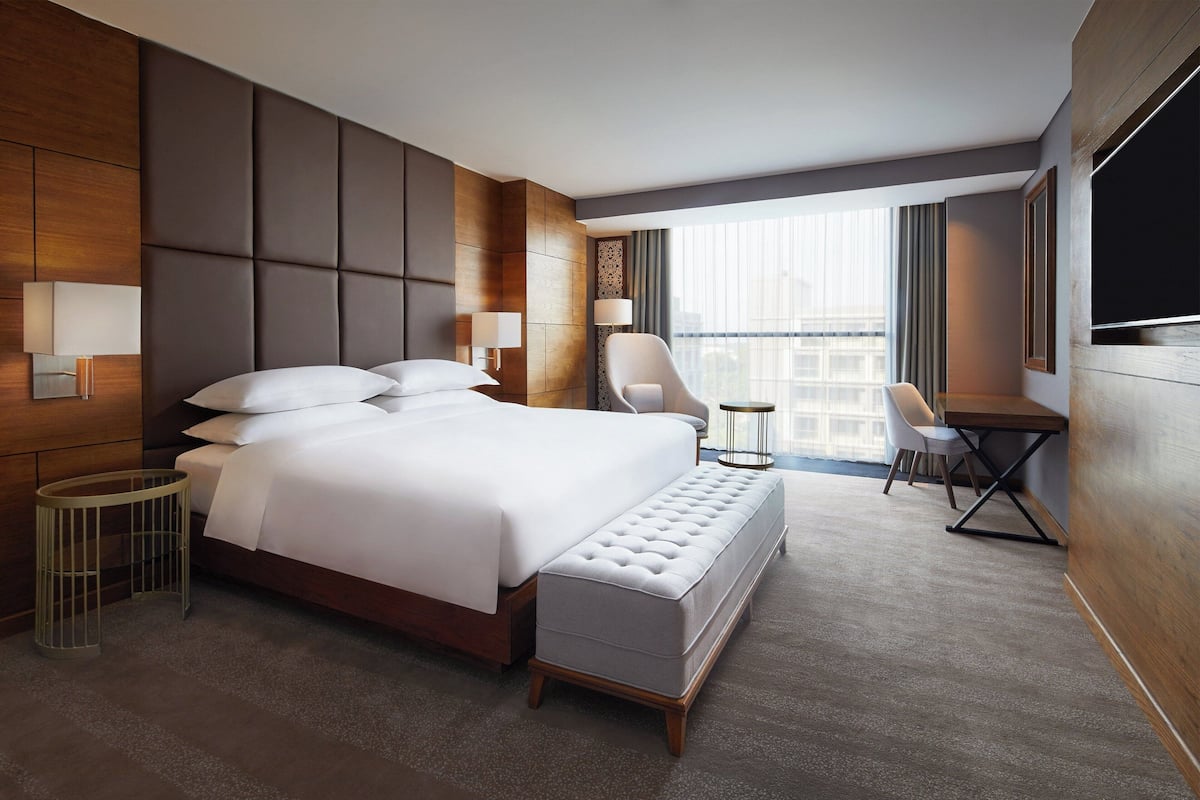 Une chambre d’hôtel moderne dotée d’un grand lit, d’un coin salon avec une chaise et une table, et d’un téléviseur fixé au mur.