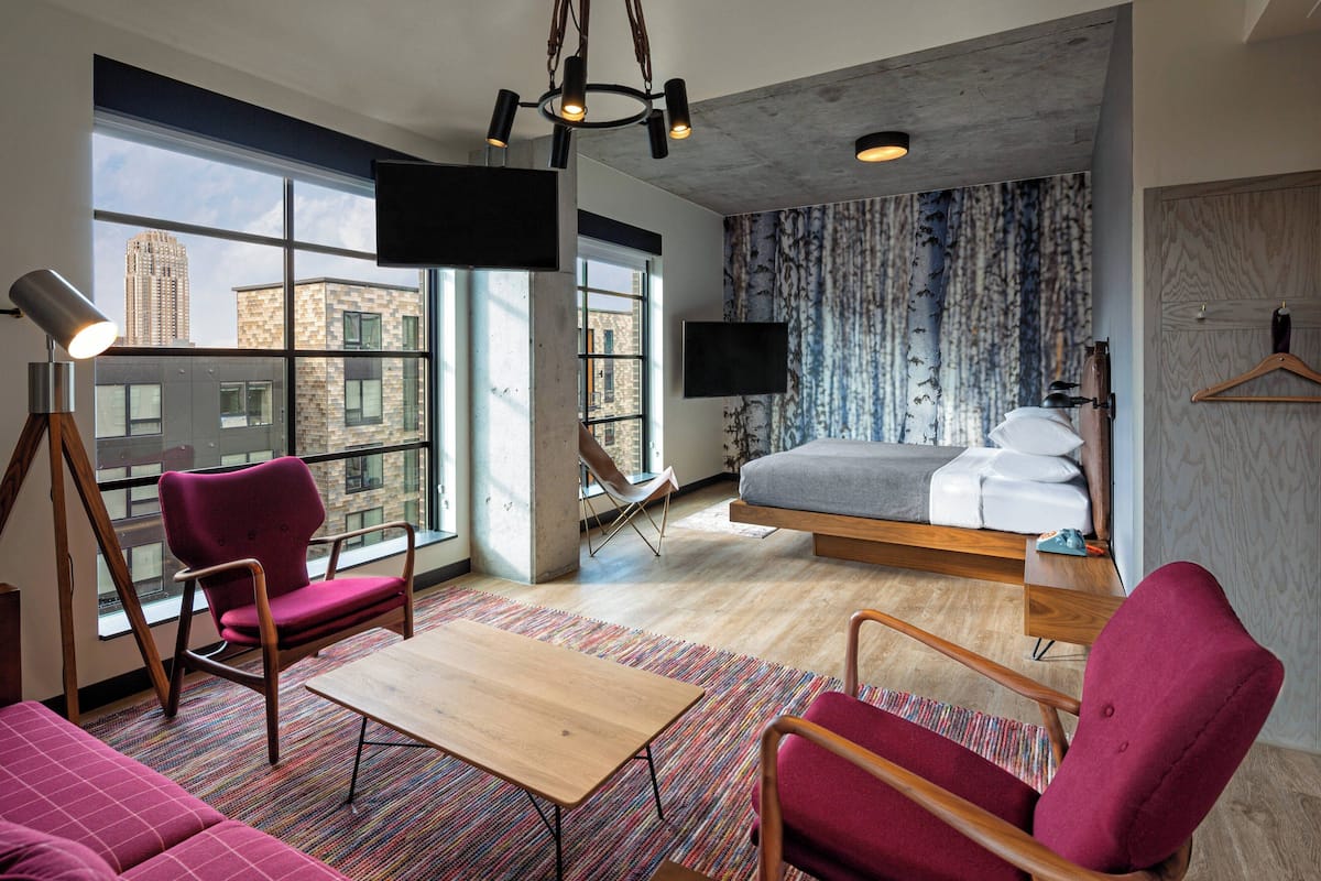 A modern hotel room with a large window, a bed, a desk, and a chair.