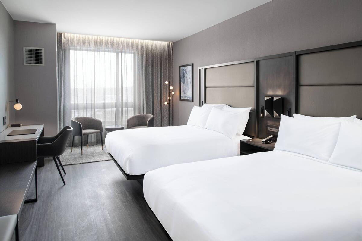 A hotel room with two beds, a desk, a chair, and a large window with curtains.