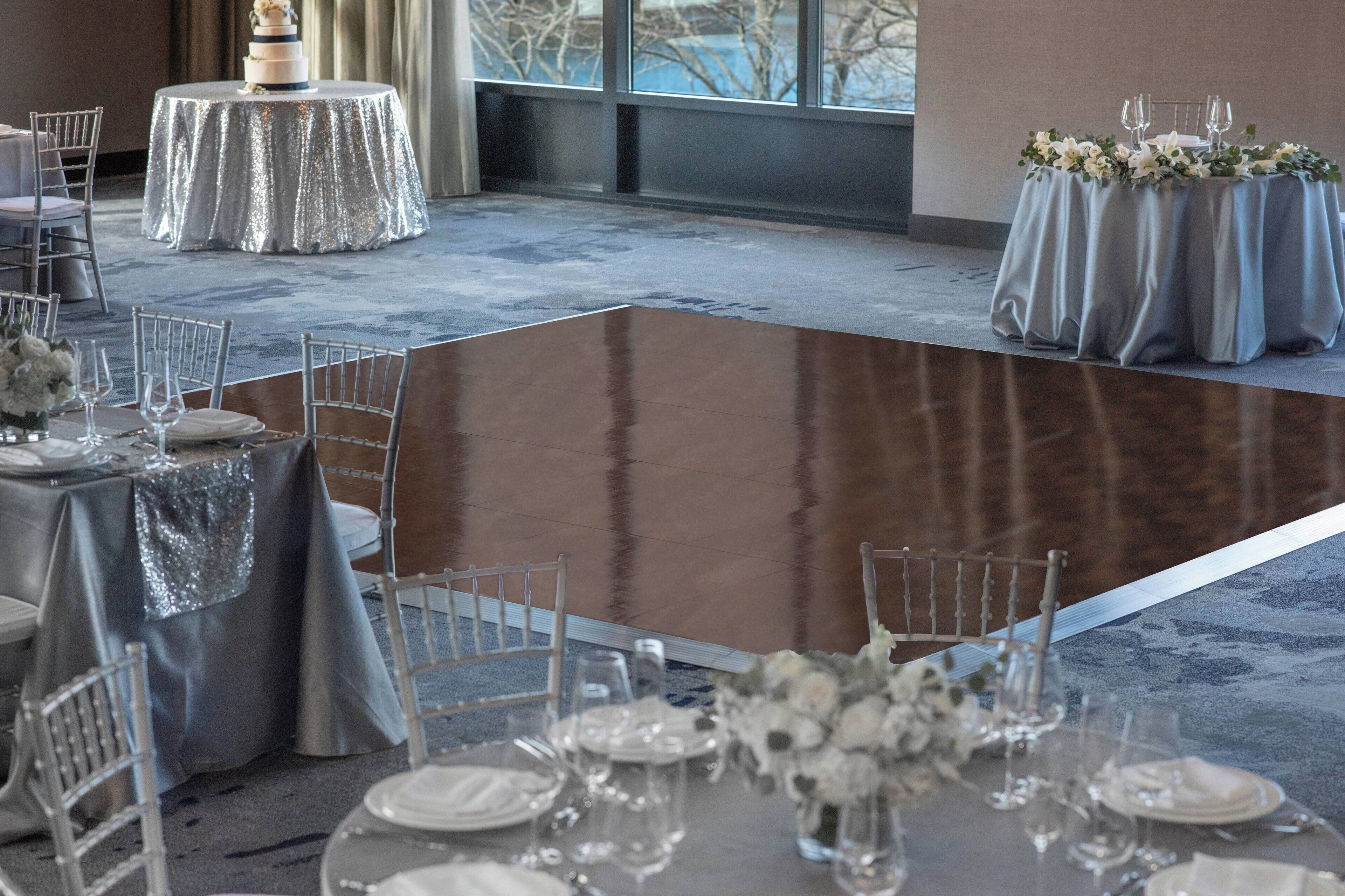 A banquet hall with round tables covered in silver tablecloths, arranged for a formal event.