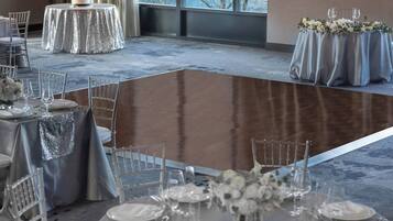 A banquet hall with round tables covered in silver tablecloths, arranged for a formal event.