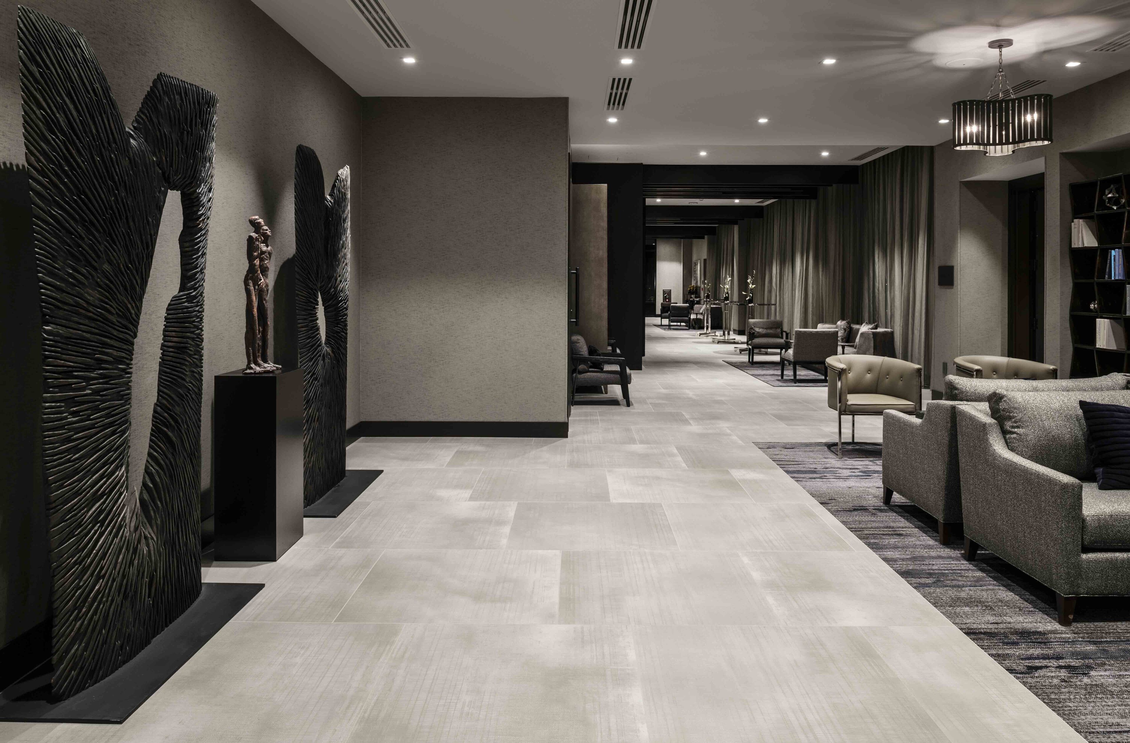 Un moderno vestíbulo de hotel con un mostrador de recepción alargado, zona de estar con sofás y sillones, y decoración mural.