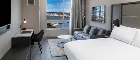A modern hotel room with a large bed, a sofa, a desk, and a view of a lake.