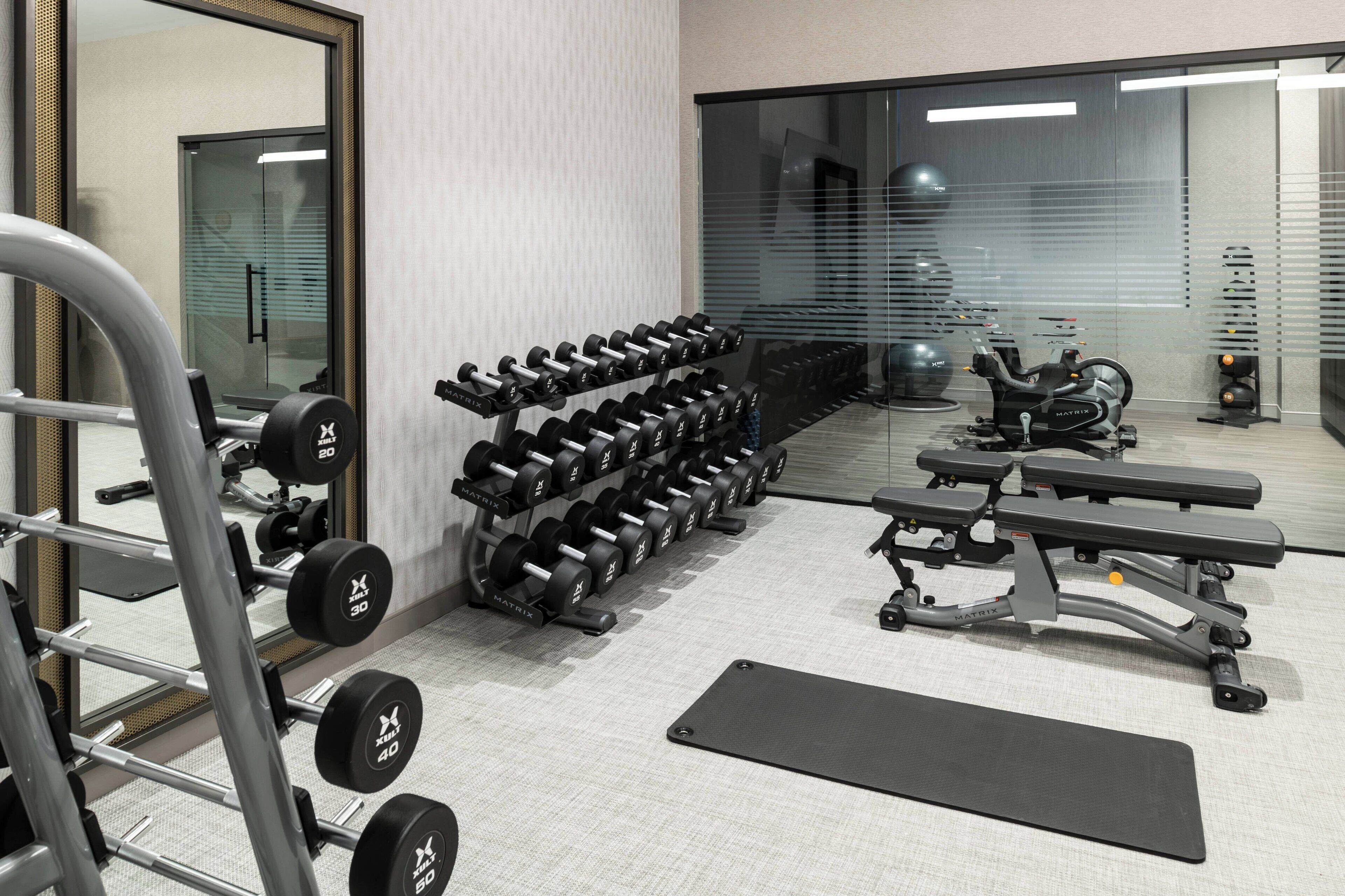 Une salle de sport équipée de matériel de musculation, de bancs et d’un miroir.