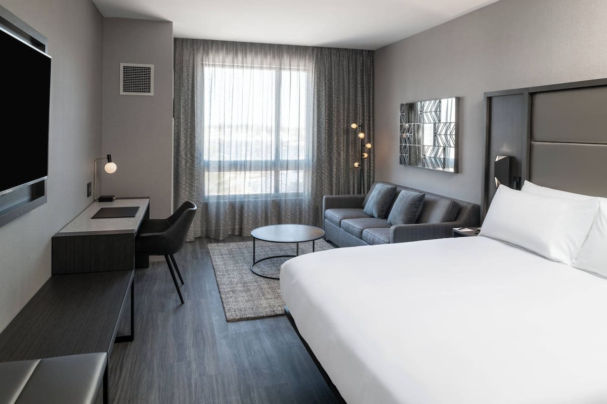 A modern hotel room with a large bed, a desk, a sofa, and a TV.