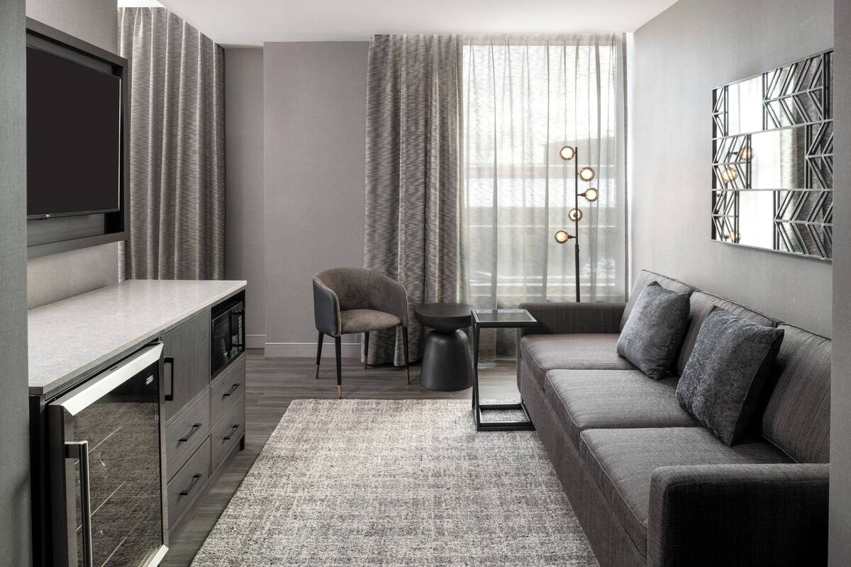 A modern living room with a flat-screen TV, a sofa, a chair, a small table, and a decorative wall piece.