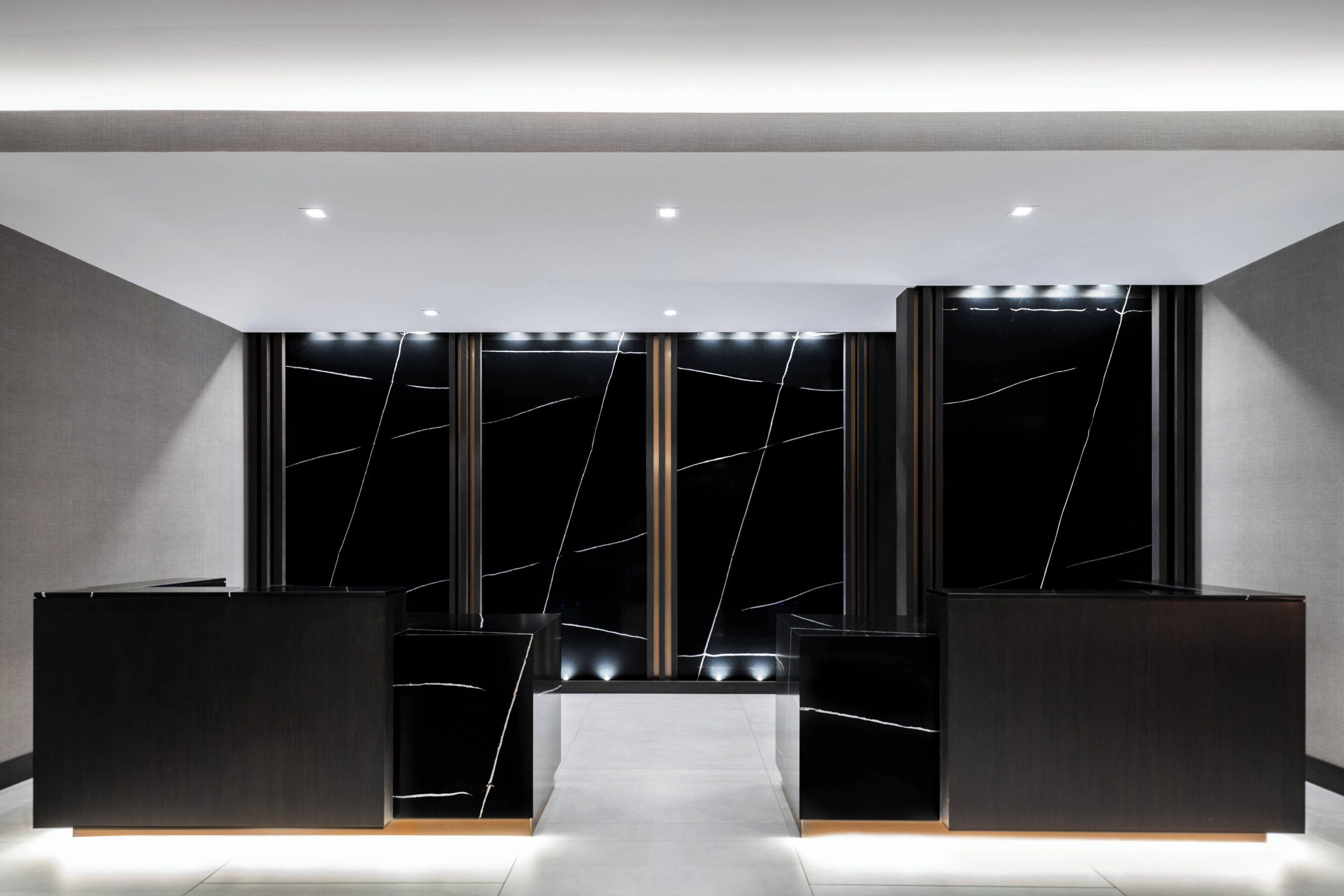 A modern reception area with a central desk, flanked by two symmetrical columns, and a dark, textured wall with a crack-like design.