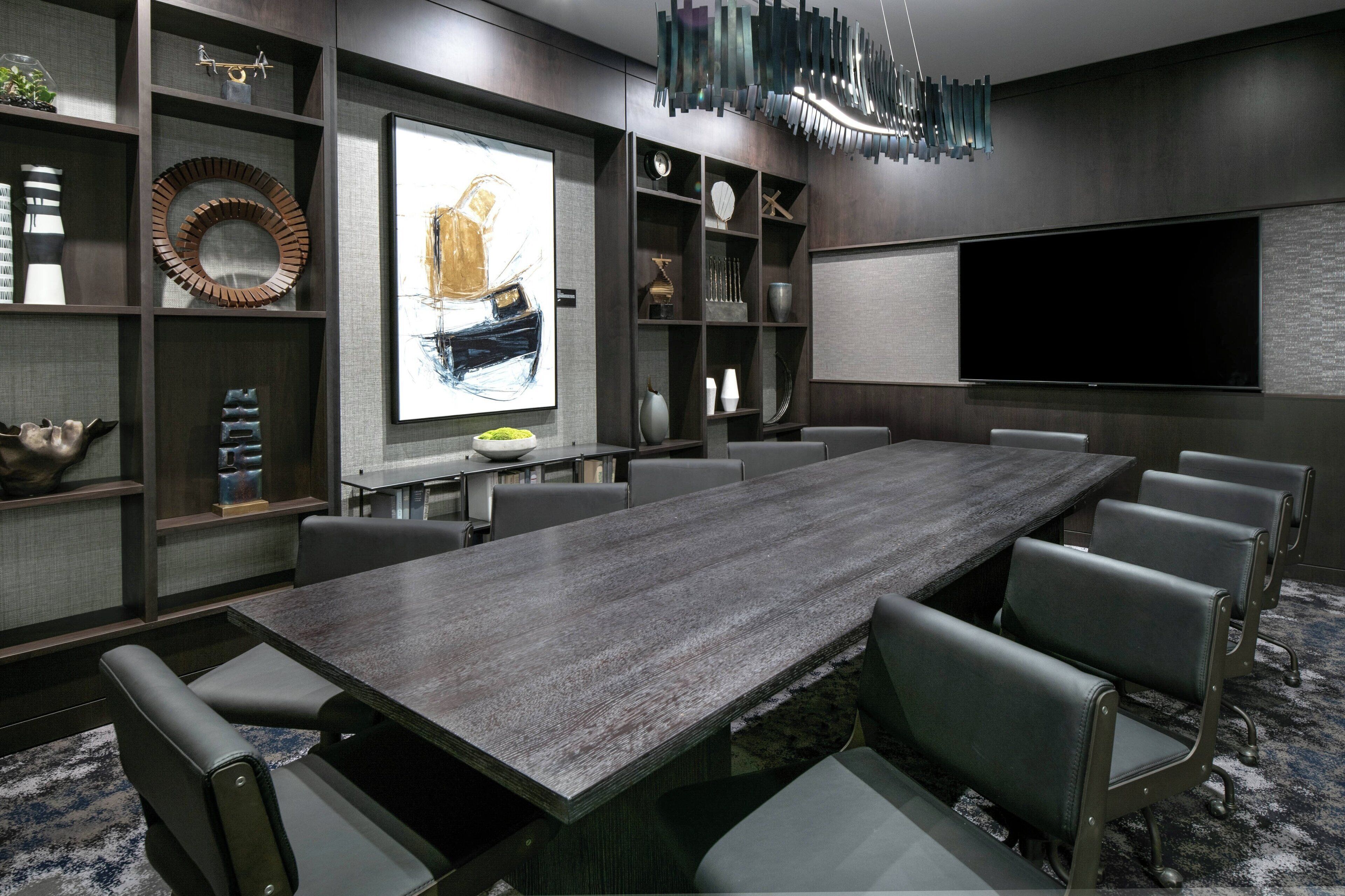 A modern meeting room with a long table, comfortable chairs, a projector screen, and decorative shelves.