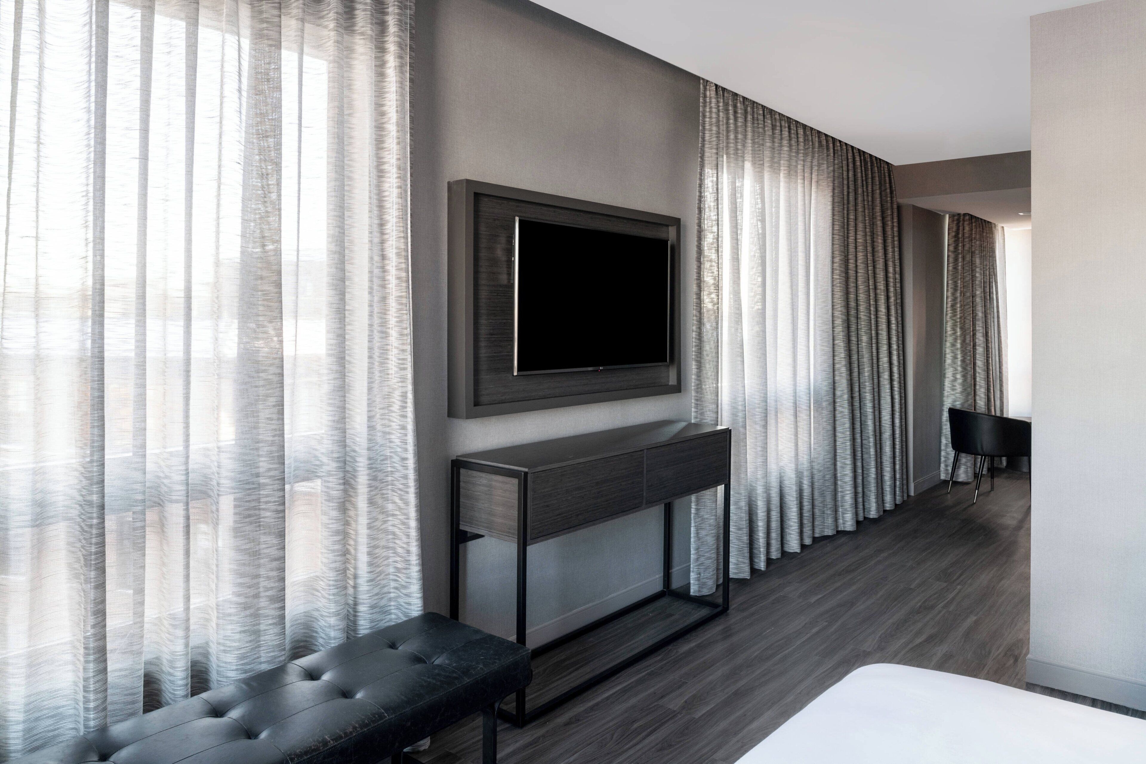 Habitació d'hotel moderna amb un gran televisor de pantalla plana fixat a una consola fosca, una panxa de seient confortable i una taula de menjador amb cadires.