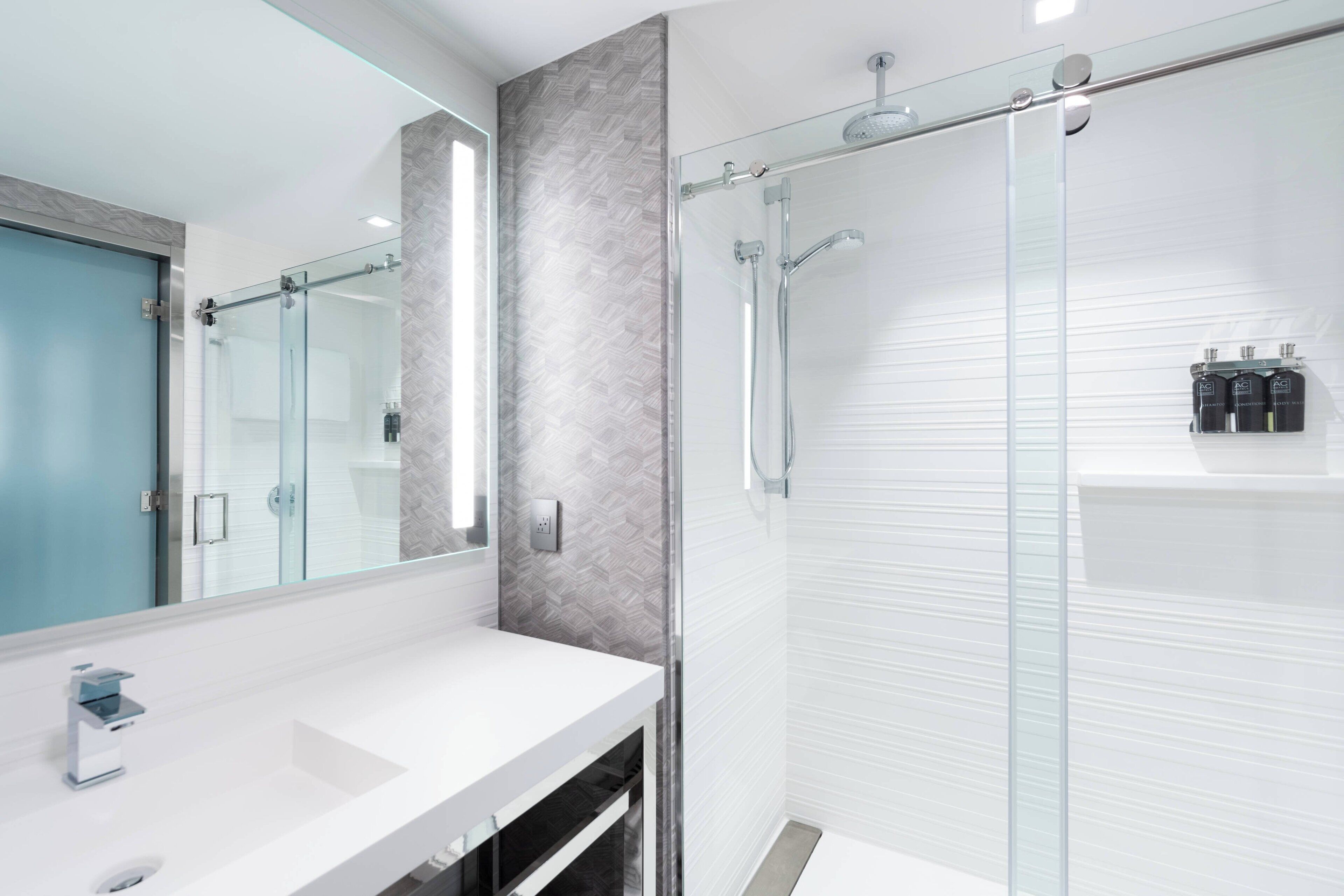 A modern bathroom with a glass shower enclosure, a white sink, and a mirror.