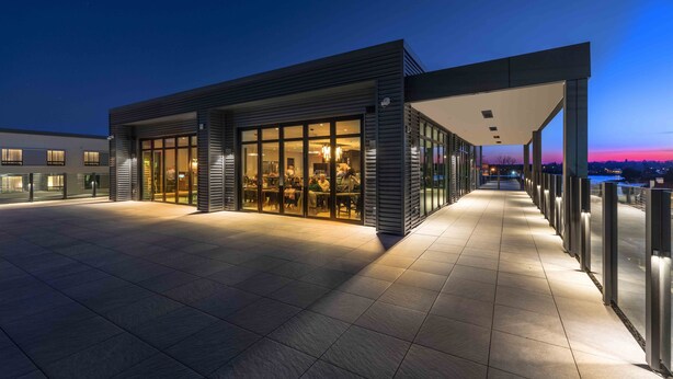 A modern building with large glass windows, a covered walkway, and a view of the cityscape at dusk. - AC Hotel by Marriott Portsmouth (Portsmouth)