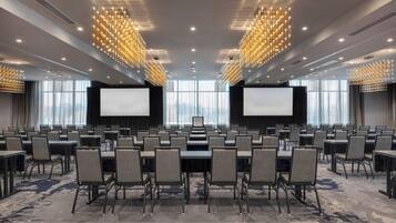 A conference room with rows of tables and chairs, large screens, and modern chandeliers.