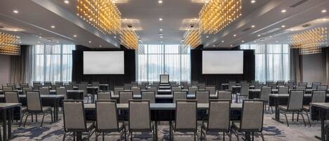 Un salón de conferencias con filas de mesas y sillas, pantallas grandes y candelabros modernos.