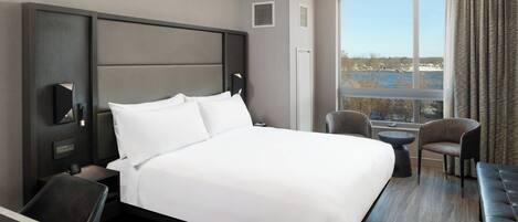 Una habitació d'hotel amb un llit gran, un escriptori, una cadira i vista a un cos d'aigua a través d'una finestra ampla.