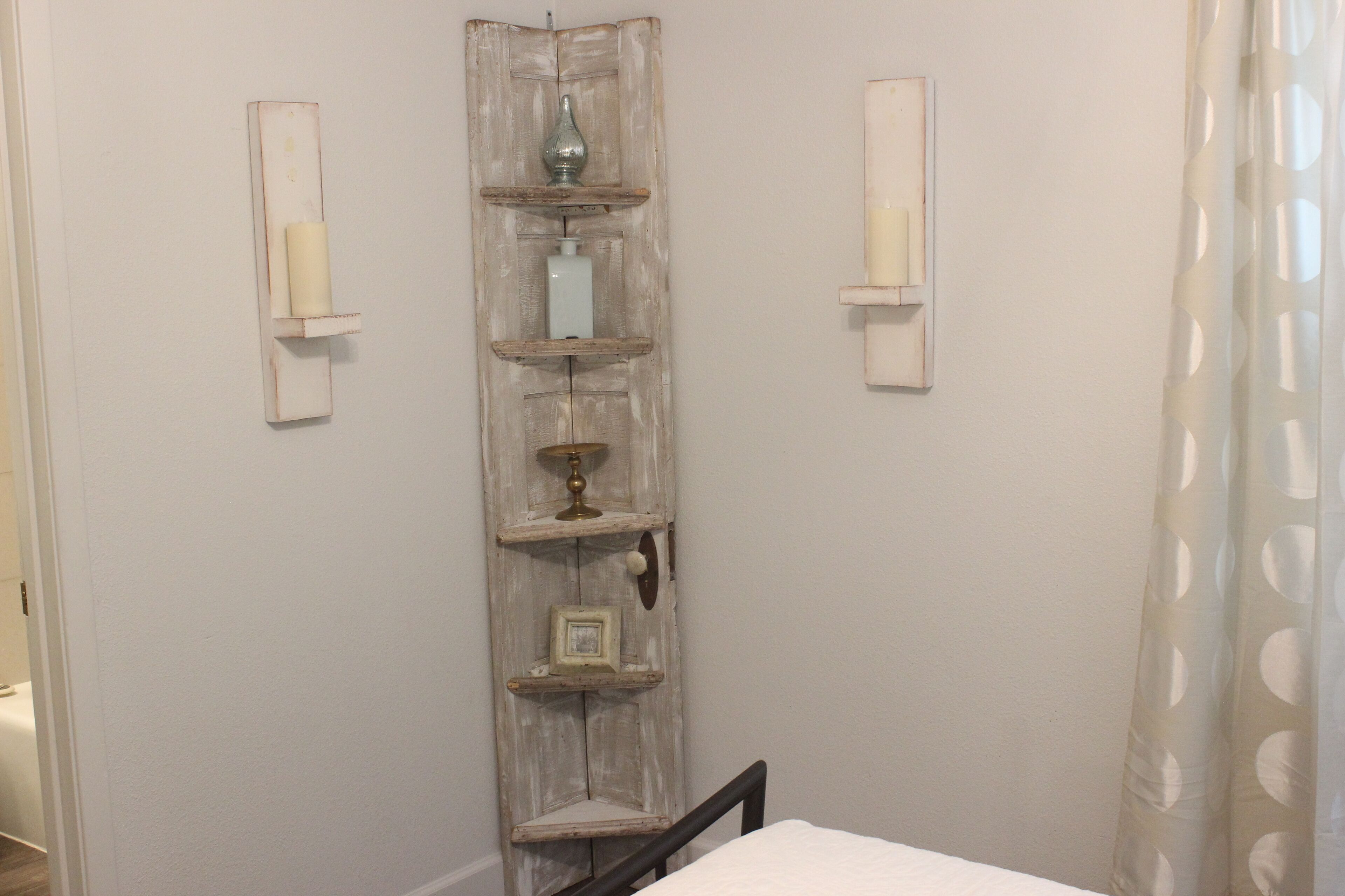 A bedroom with a bed, a wooden shelf unit with decorative items, and a white wall.