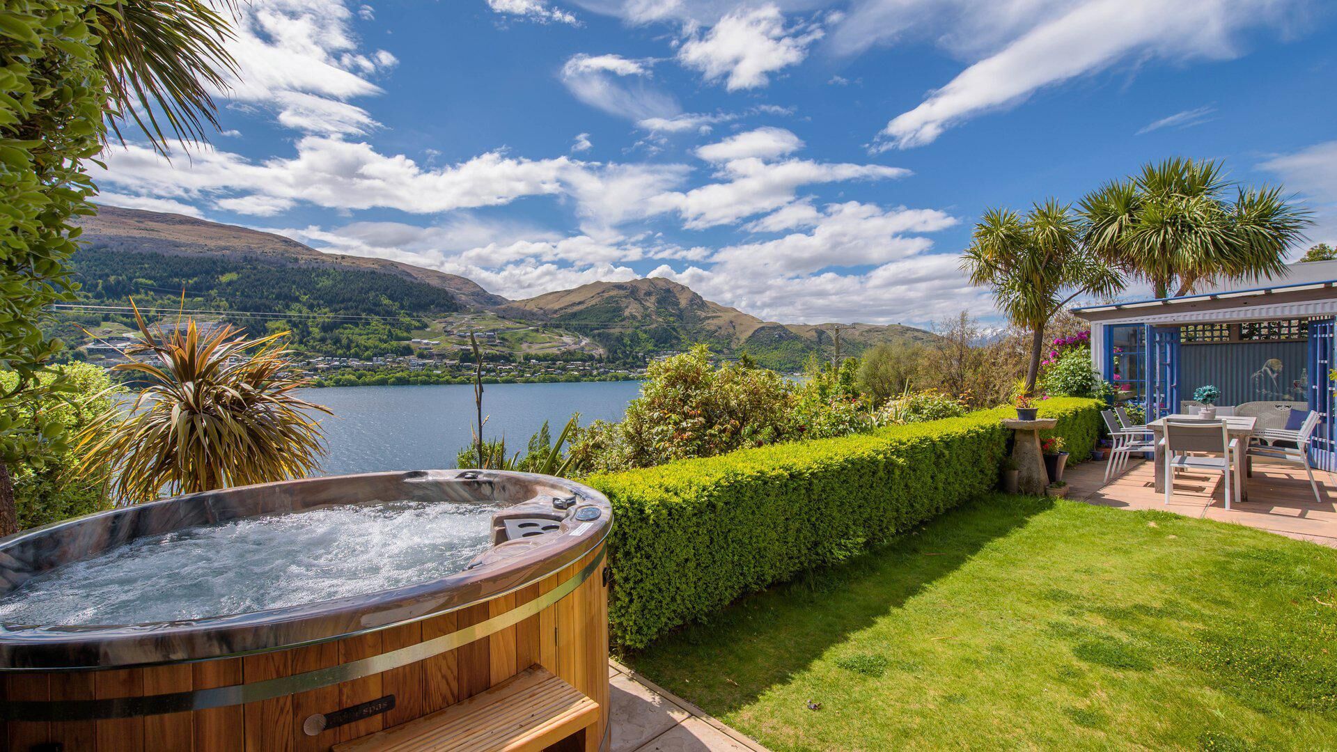 A hot tub in a garden with a view of a lake and mountains.