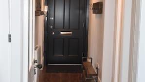 Un pasillo estrecho con una puerta de madera oscura, un banco y una lámpara colgante.