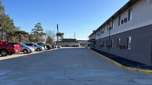 Un estacionamiento con varios coches, un edificio de múltiples ventanas y techo plano, y un cielo azul despejado.