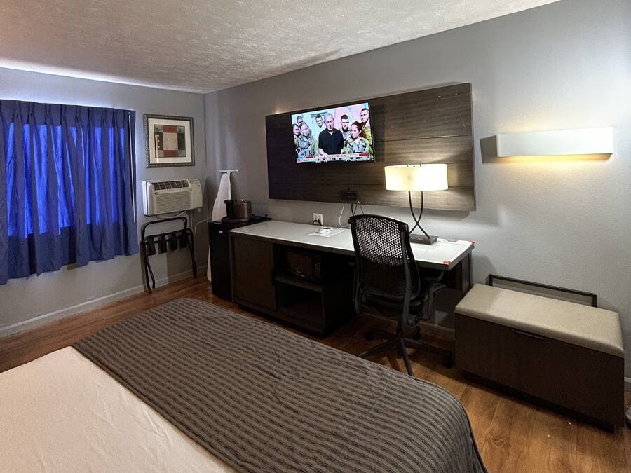 Una camera d'albergo con un letto, una scrivania, una sedia, una TV e un tavolino.