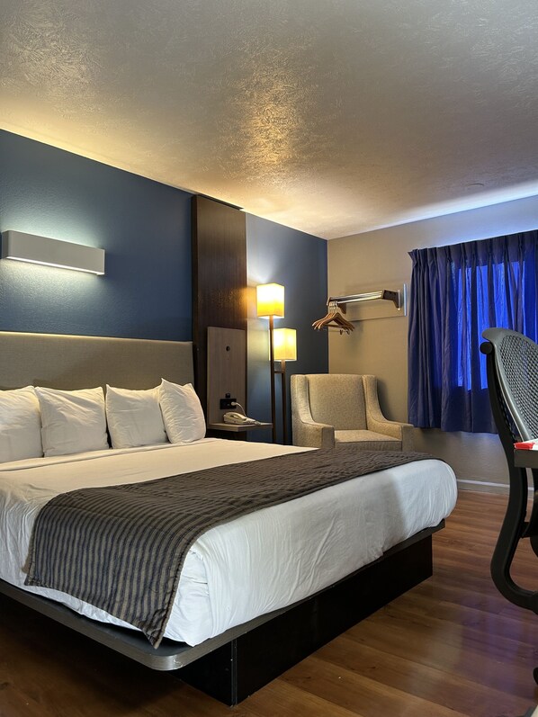 A hotel room with a large bed, bedside tables, a chair, a lamp, and a window with curtains. - Rodeway Inn Emporia (Emporia)