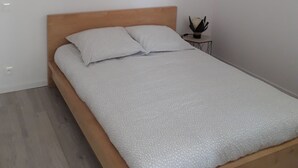 Une chambre à coucher avec un lit en bois, une couvre-lit blanche à motifs, une petite table de chevet avec une plante et un luminaire suspendu.