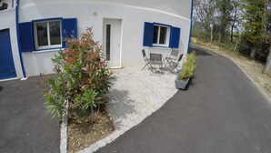 Un bâtiment avec des volets bleus, une entrée pavée et des places assises à l’extérieur.