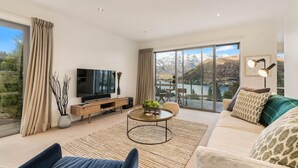 A modern living room with a large TV, a sofa, a coffee table, and a view of mountains through large windows. - Quaint Sanctuary on Quartz | Incredible Views | (Queenstown)