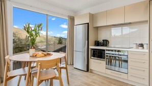A modern kitchen with a large window, a dining table with chairs, and a view of a hillside. - Quaint Sanctuary on Quartz | Incredible Views | (Queenstown)