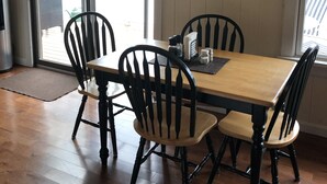 A dining area with a wooden table and four chairs, a painting on the wall, and a view of a lake through large windows. - Welcome to Heav'nsent (Swanville)
