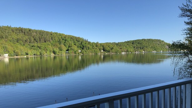 A calm lake with a wooden dock extending into the water, surrounded by lush green hills and clear blue sky. - Welcome to Heav'nsent (Swanville)